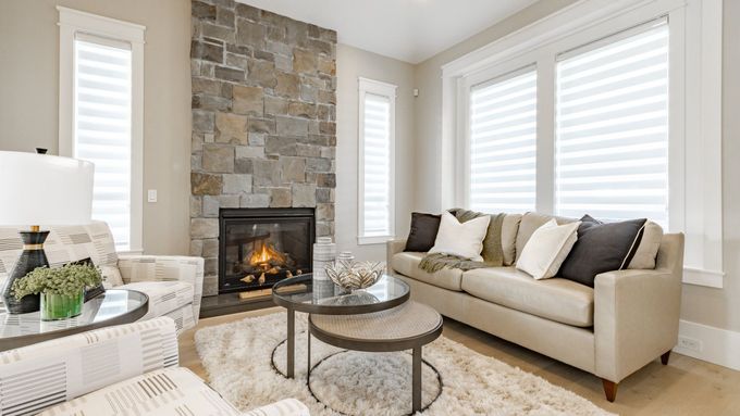 Modern living room with green sofa, fireplace, large wall TV, and wooden chairs near bright windows.
