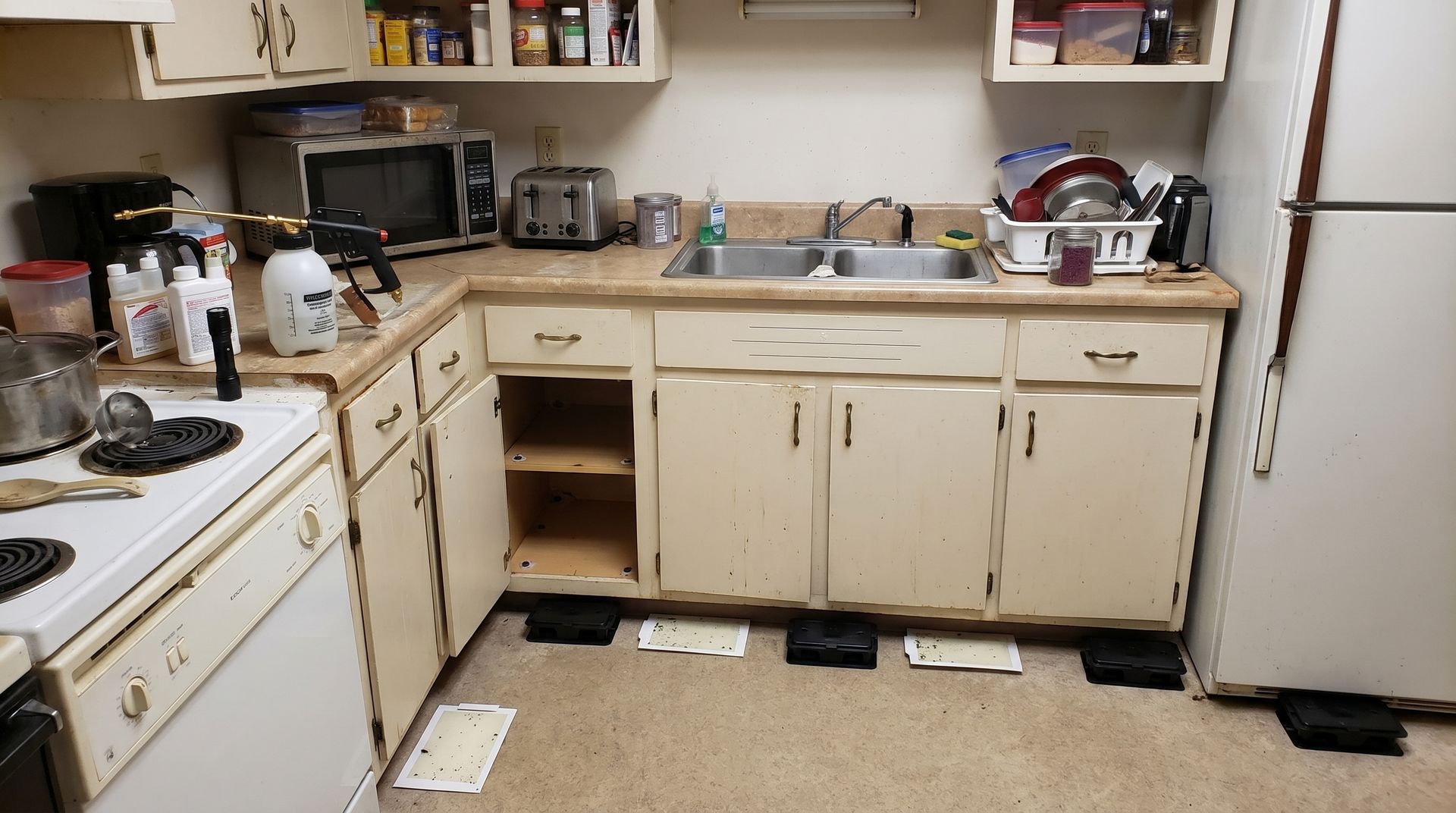 Small kitchen with cream cabinets, white appliances, and a sink under open shelves.