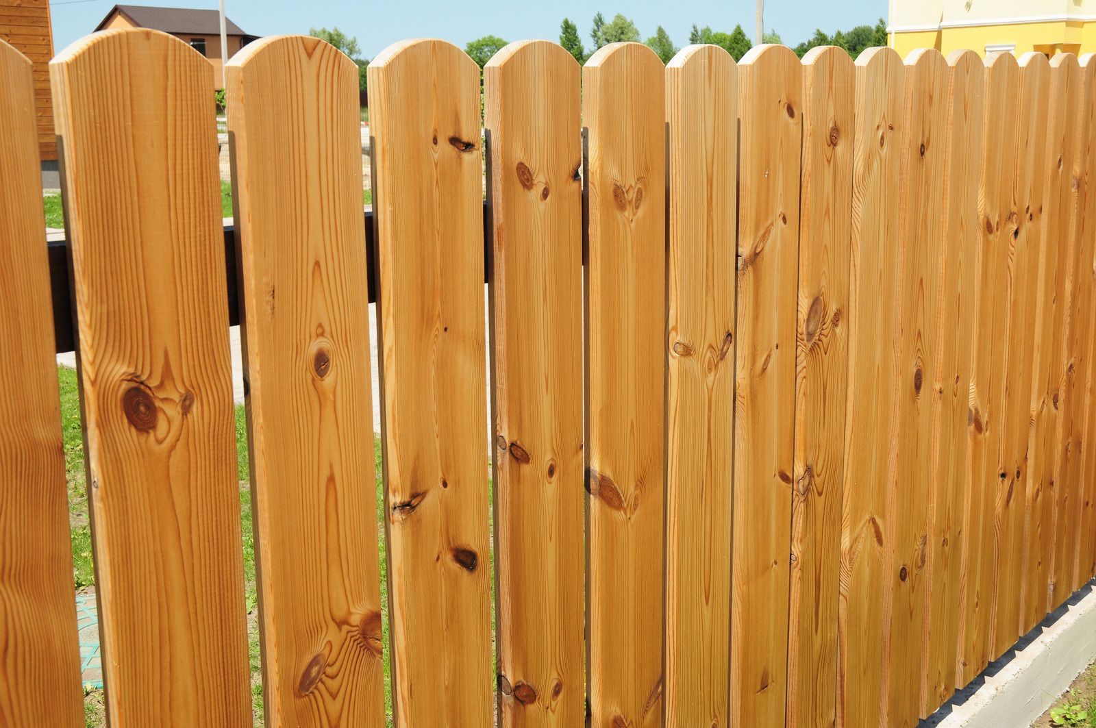 Wooden picket fence, stained light brown, outdoors.