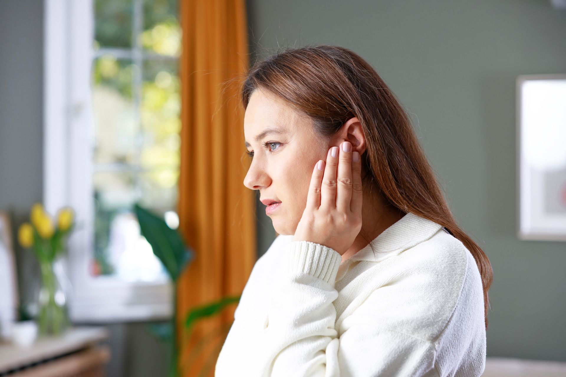 A young woman holding her left ear with ear pain at home.