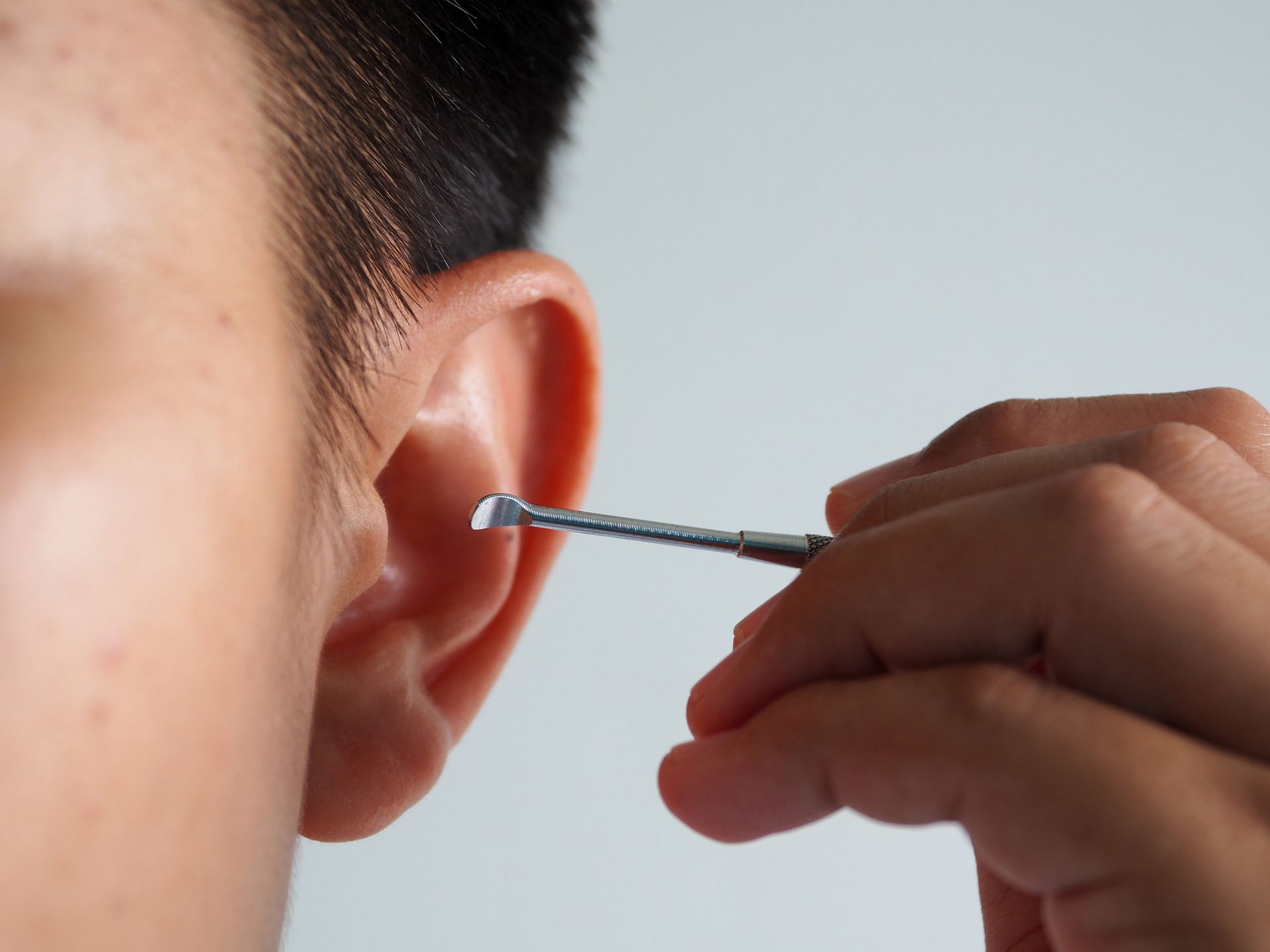 Close-up of ear being cleaned with a small metal tool held by a person's hand.