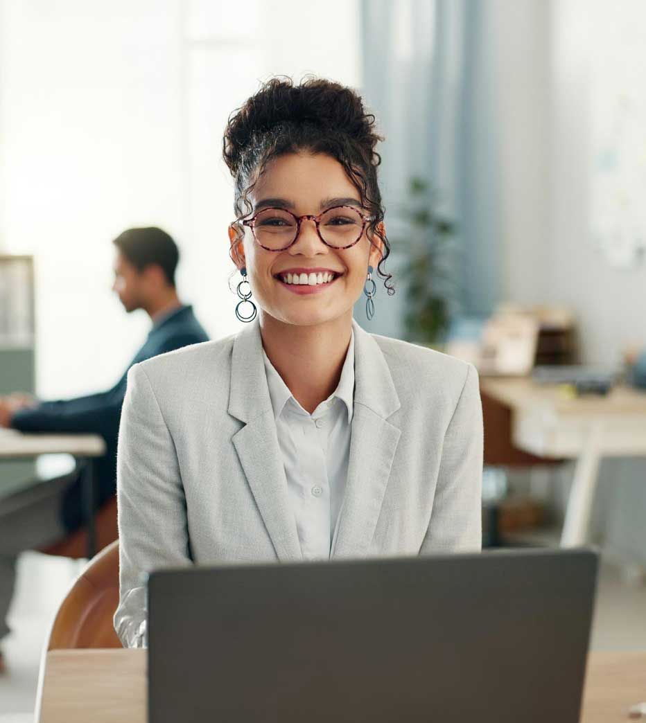 A woman is smiling while sitting in front of a laptop computer.