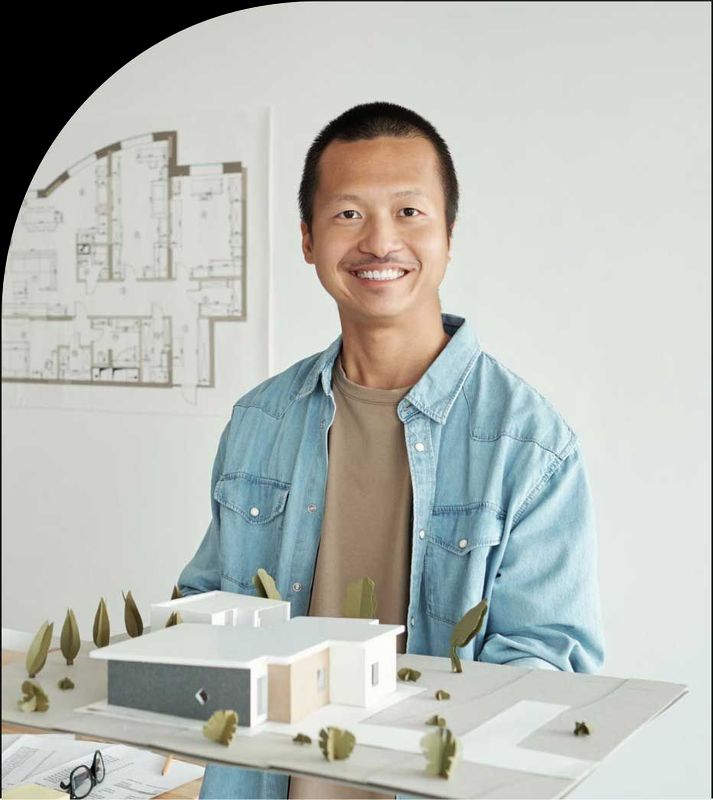 A man in a blue shirt is holding a model of a house.