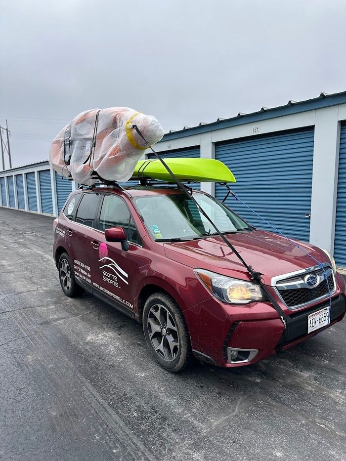 A red subaru forester with a yellow kayak on top of it.