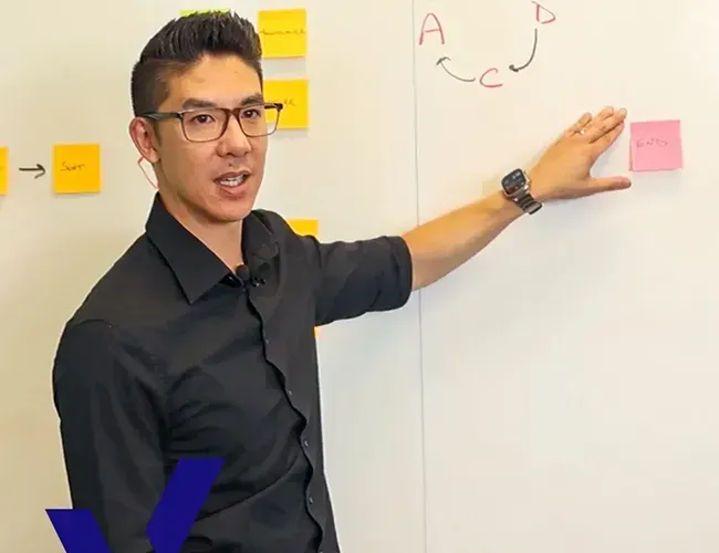Man in black shirt pointing at sticky notes on a whiteboard during a presentation