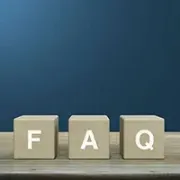 Wooden blocks spelling “FAQ” on a shelf against a blue wall.
