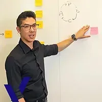 Man in black shirt pointing at pink sticky note on a whiteboard with a circular sketch and yellow notes