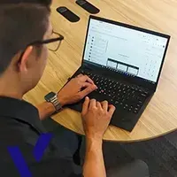 Person using a laptop at a wooden table, viewing a chart or dashboard on the screen.