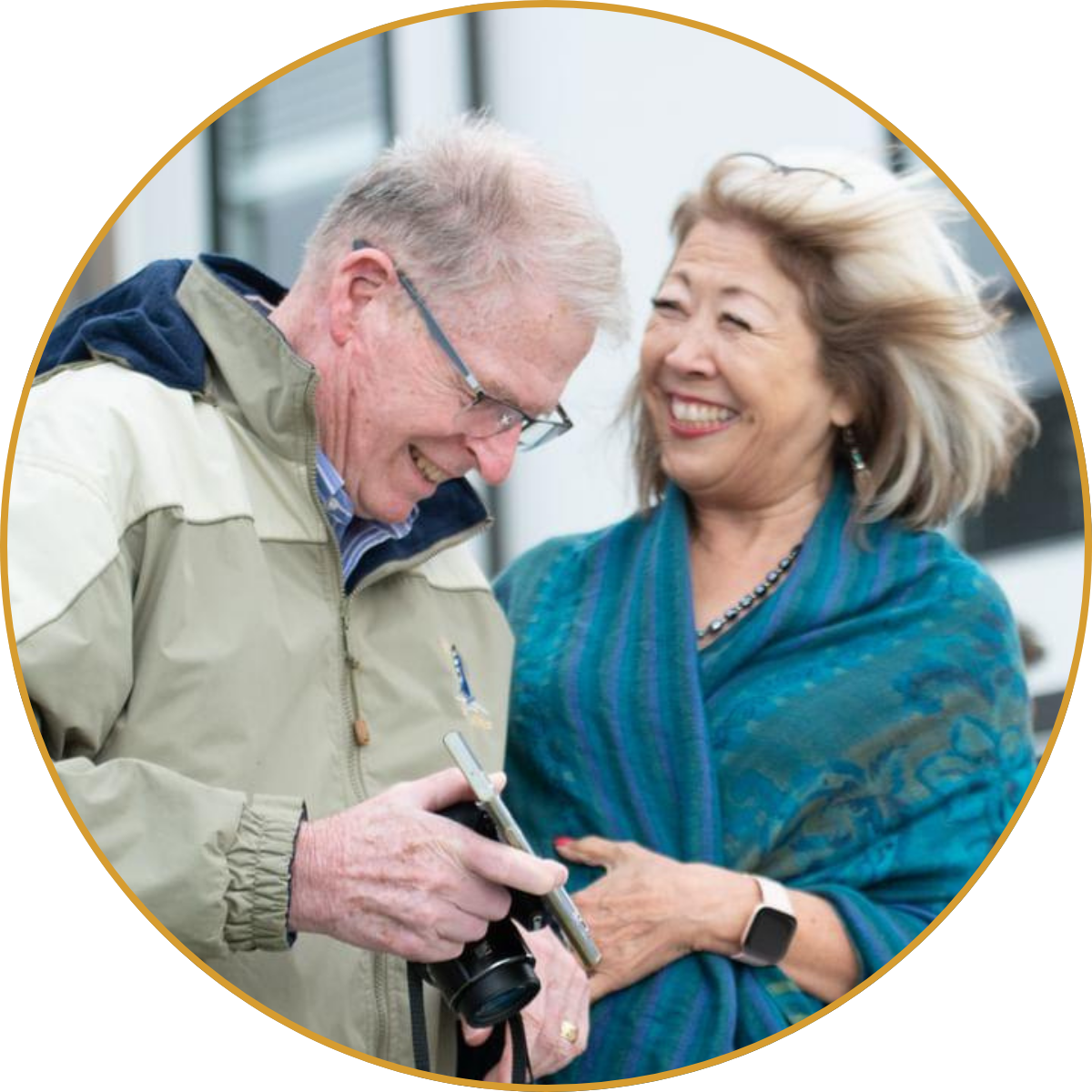 Smiling couple looking at a camera, with the man holding it and the woman in a blue scarf beside him.