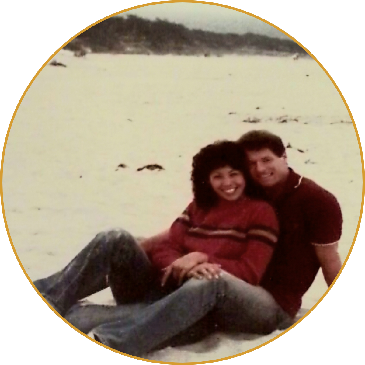 Two people sitting close together on a snowy field, smiling at the camera.