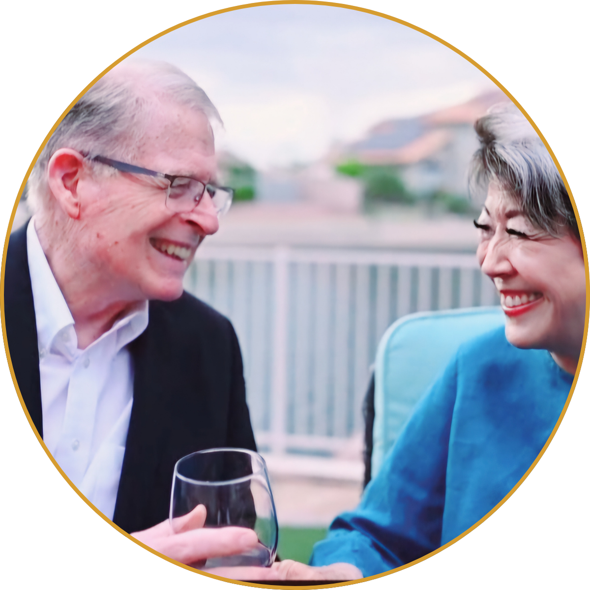 Two people smiling and toasting with glasses on a patio, framed in a circular border.