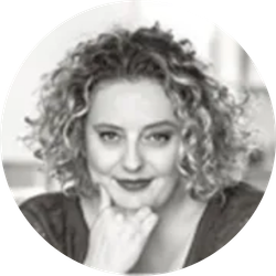 Black-and-white portrait of a person with curly hair, resting their chin on their hand and smiling softly