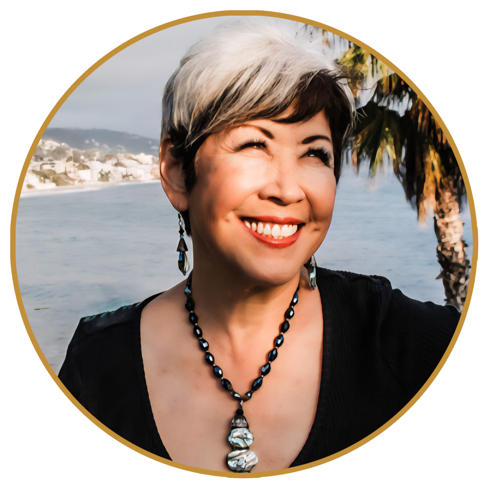 Smiling person with short gray hair, black top, and beaded necklace, with a coastal view behind.