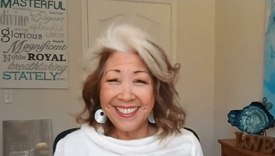 Smiling person in a white top with a sign and blue decor in the background