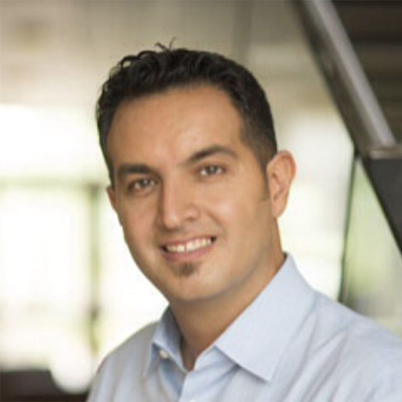 Smiling person in a light blue shirt indoors, with a softly blurred background
