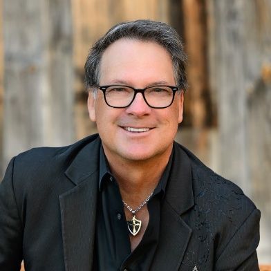Smiling man in black jacket and glasses against a blurred wooden background