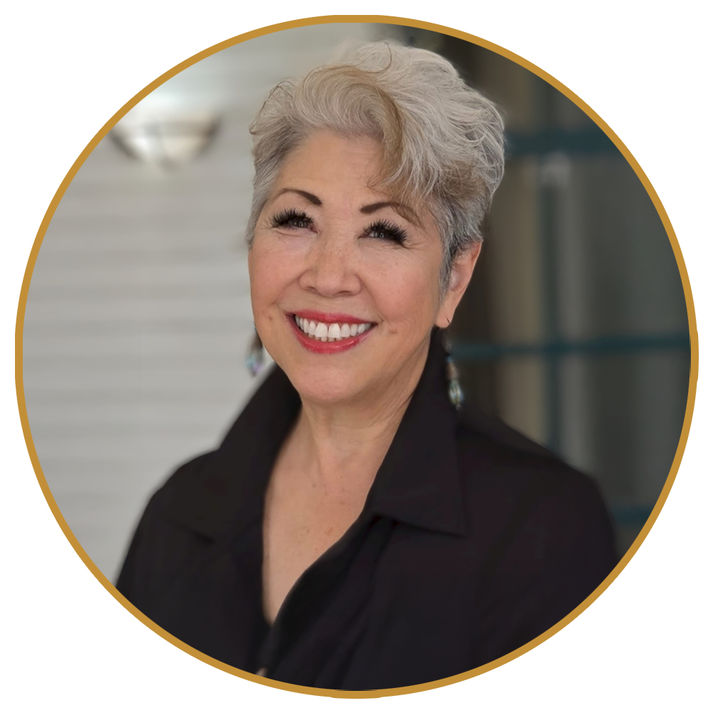Smiling woman with short silver hair in a black top against a blurred background, framed by a gold circle