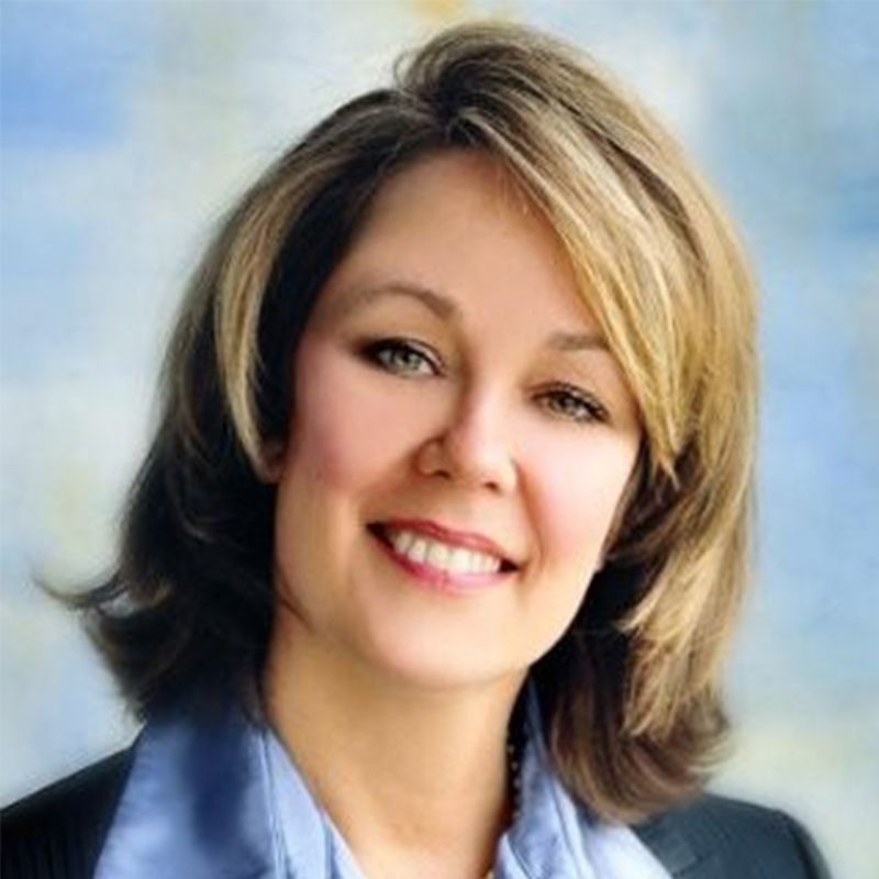Smiling woman with shoulder-length blonde hair in a blue blazer against a softly blurred background
