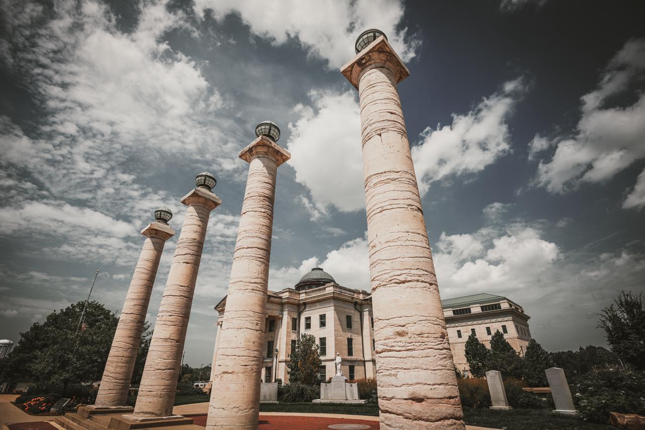 Four tall columns stand before a large building under a cloudy sky.