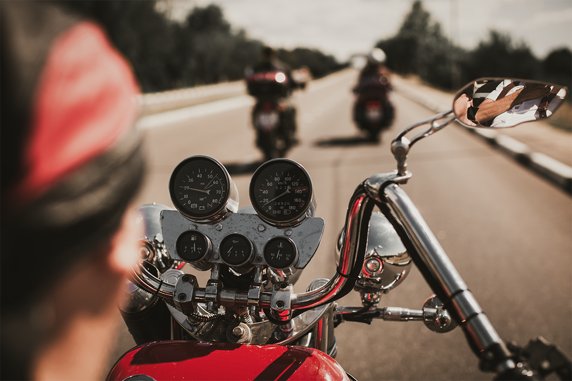 Motorcycle rider’s view on a highway, with red bike dashboard and two motorcycles ahead under a partly cloudy sky