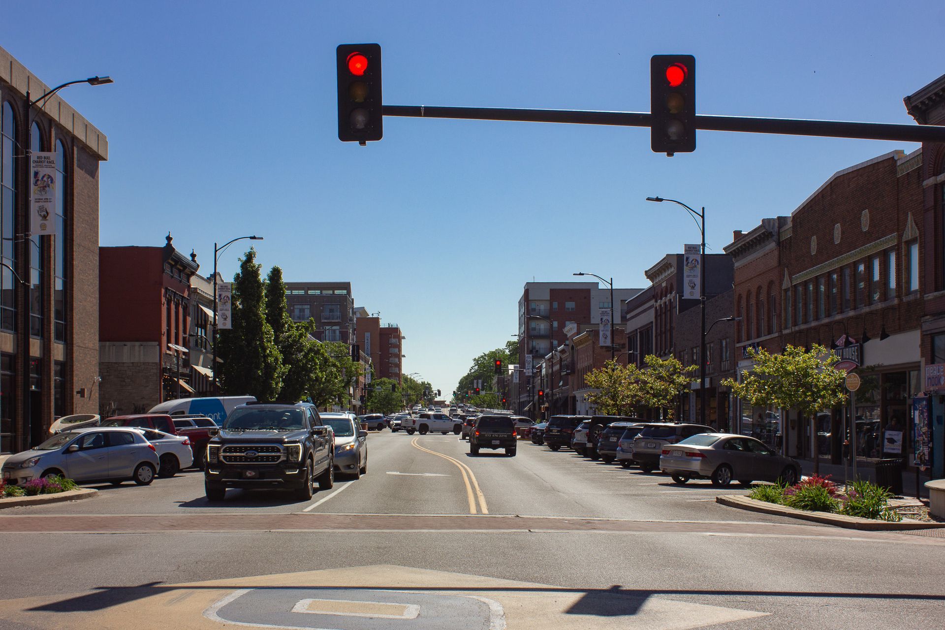 Downtown street with red traffic lights, parked cars, and brick storefronts on a sunny day