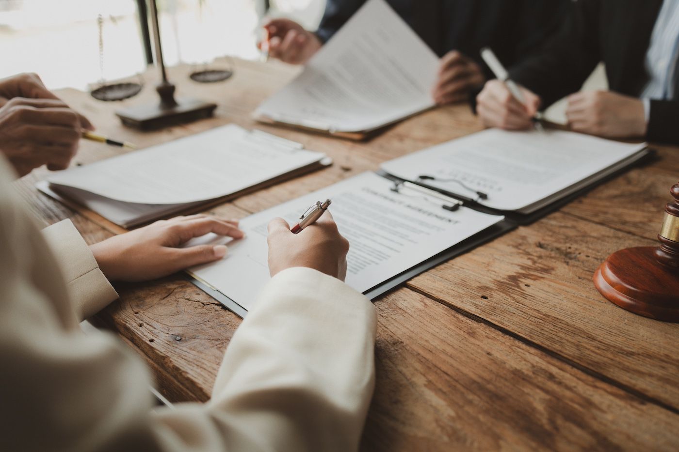 People reviewing documents and signing papers at a wooden meeting table
