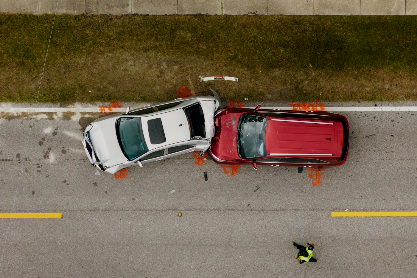 Overhead view of a white car and red SUV crashed on a roadside, with debris scattered nearby.