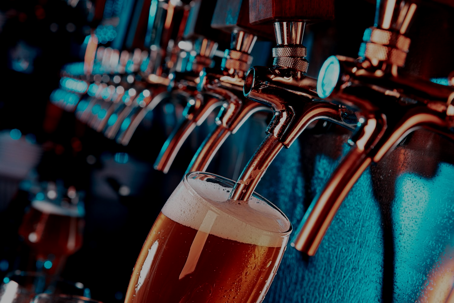 Beer taps pouring amber draft beer into a glass in a dimly lit bar