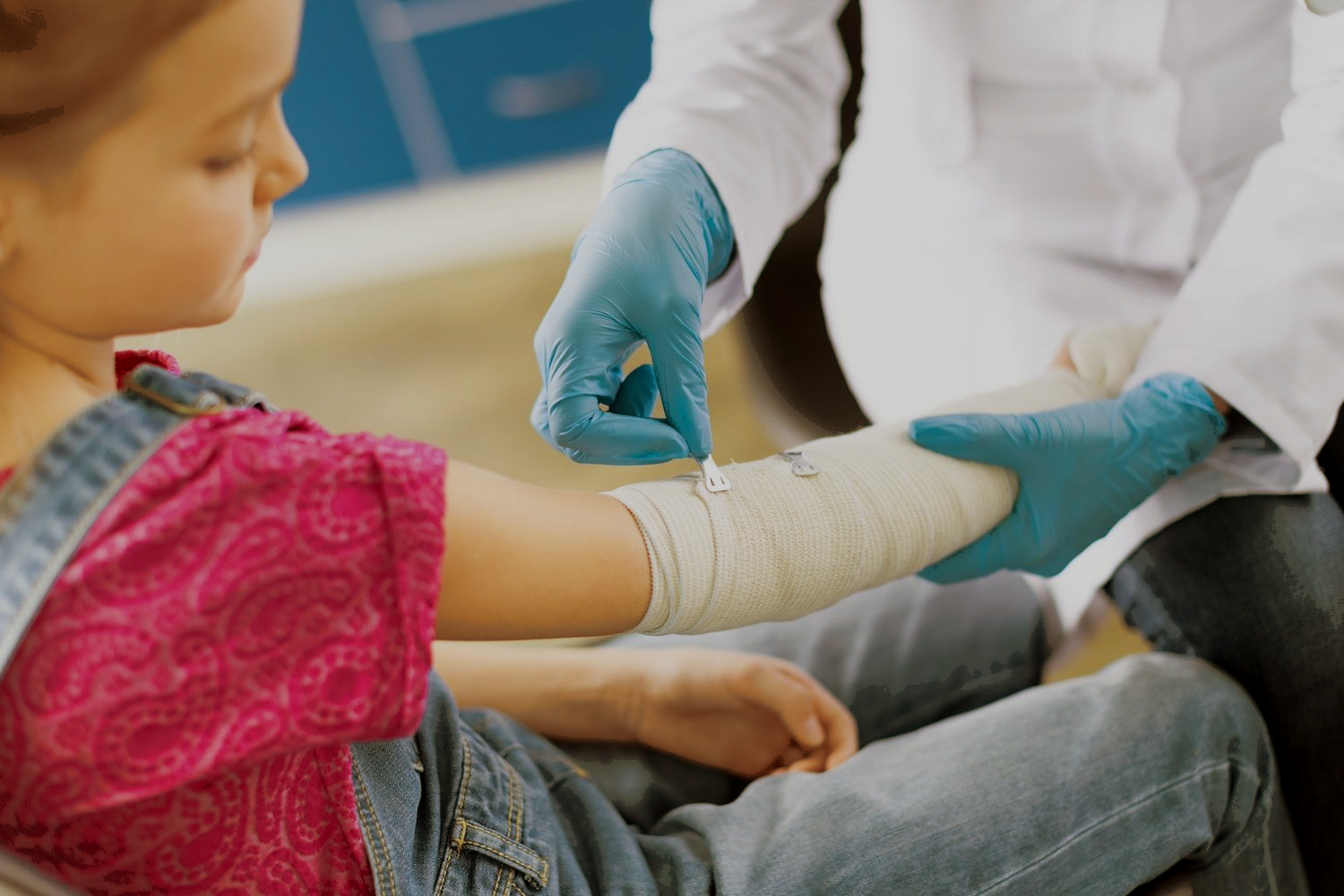 Child receiving a bandage on an arm from a healthcare worker wearing blue gloves