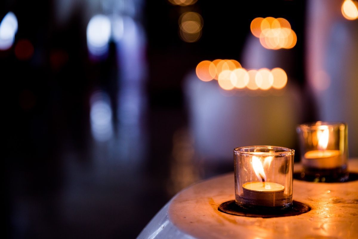 Two funeral candles flicker in the foreground with more in candles in the background