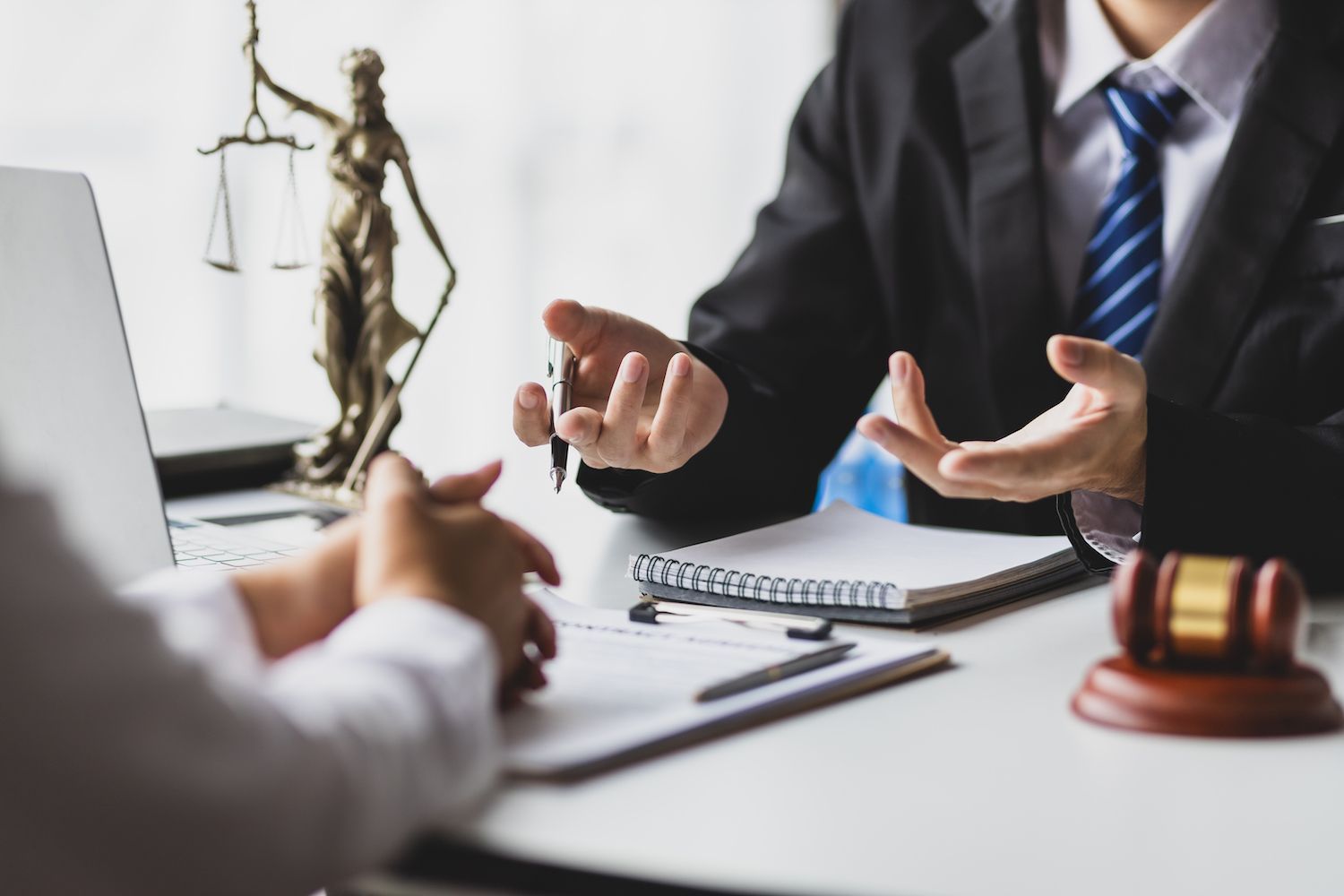 Lawyer in suit discussing a case across a desk with scales, gavel, and notebook nearby