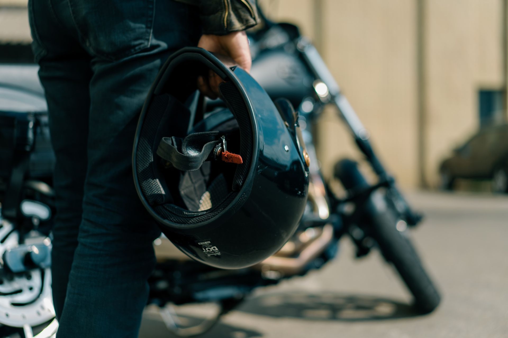 Person holding a black motorcycle helmet beside a parked motorcycle outdoors