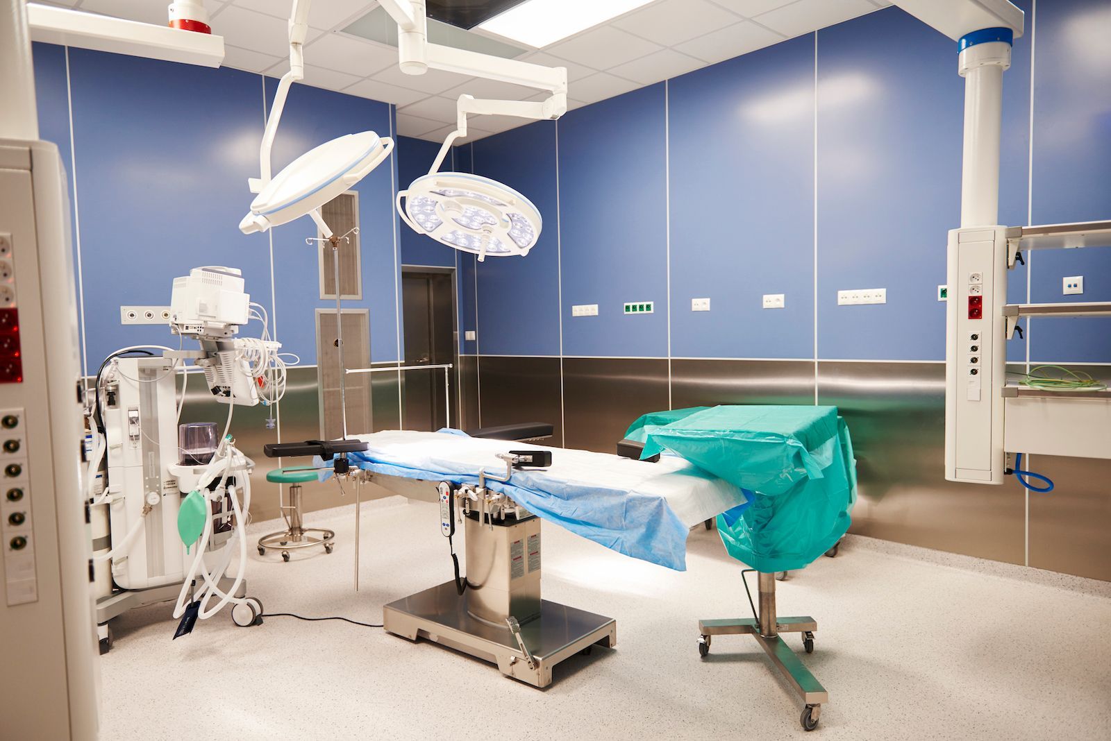 Empty hospital operating room with surgical table, overhead lights, monitors, and medical equipment