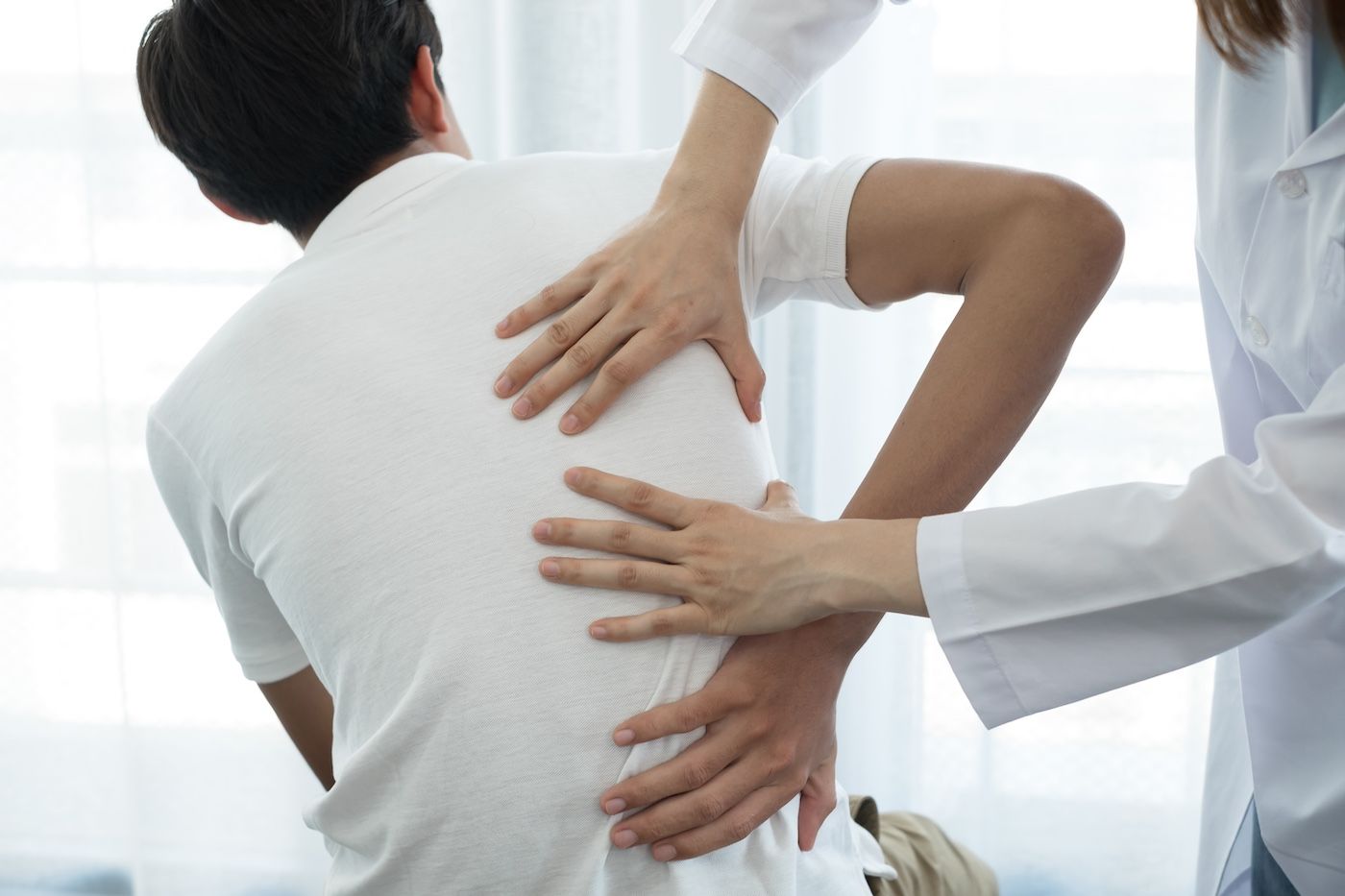 Doctor examining a patient’s back with hands on the spine in a bright clinic