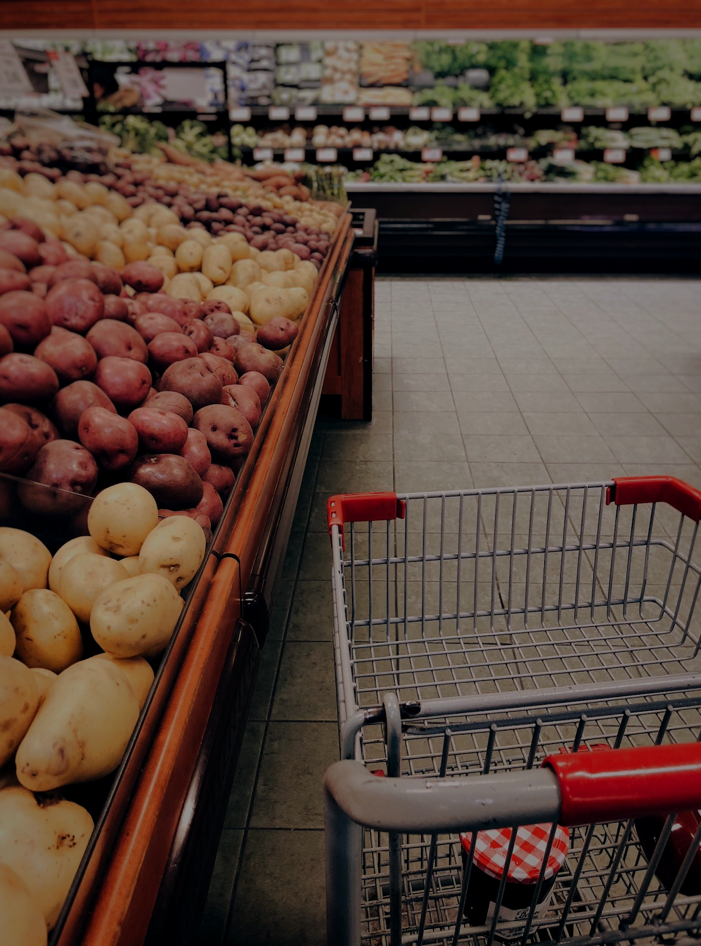 Shopping cart in a grocery store aisle beside a display of potatoes and other produce