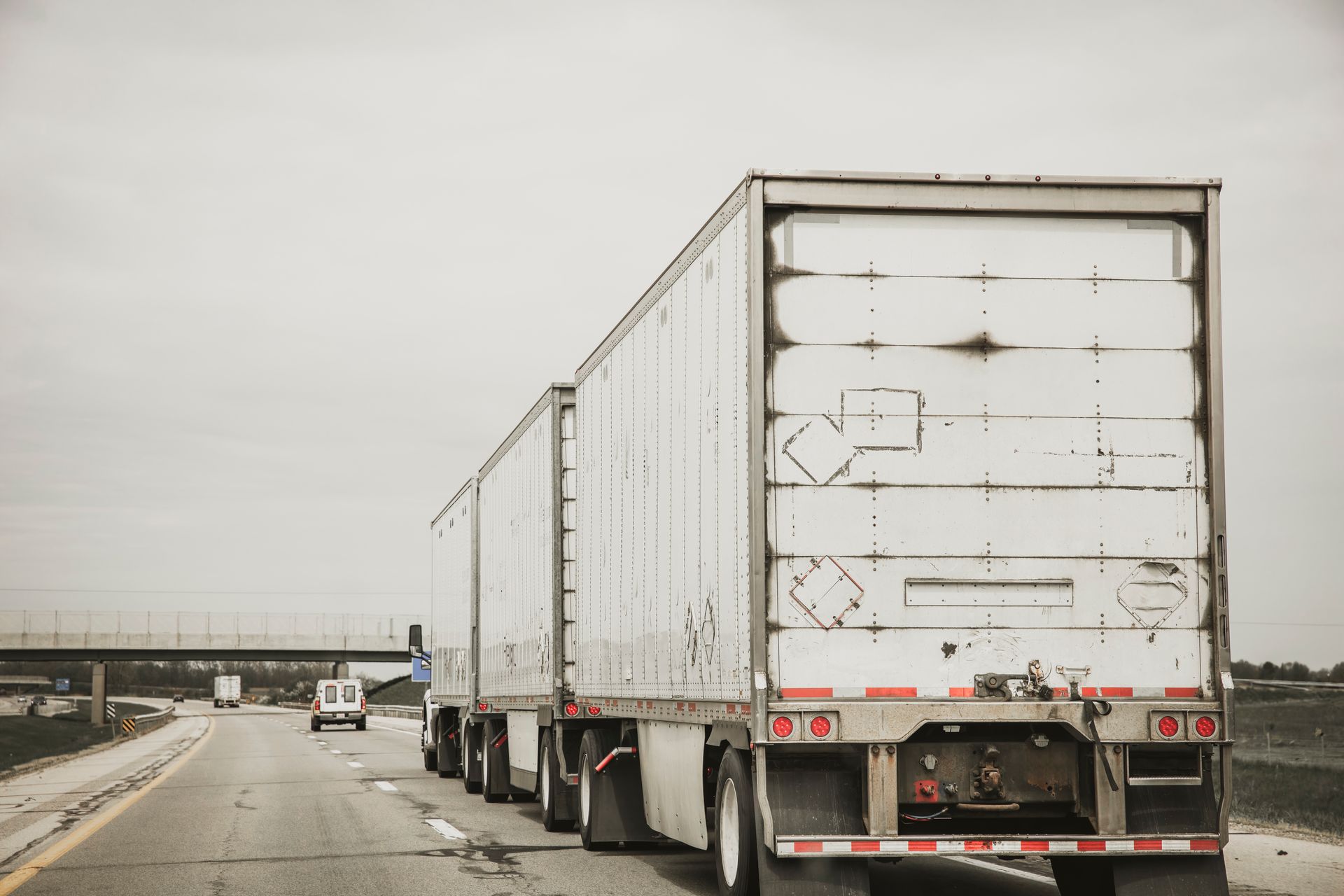 Two white semi-trucks driving on a wet highway under a gray sky