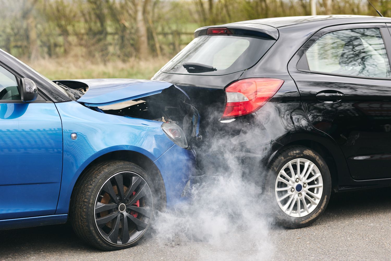 Blue car rear-ending black car on a road, with smoke rising from the impact.