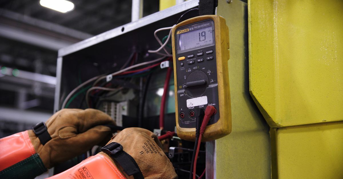 A man is using a multimeter to test an electrical outlet.