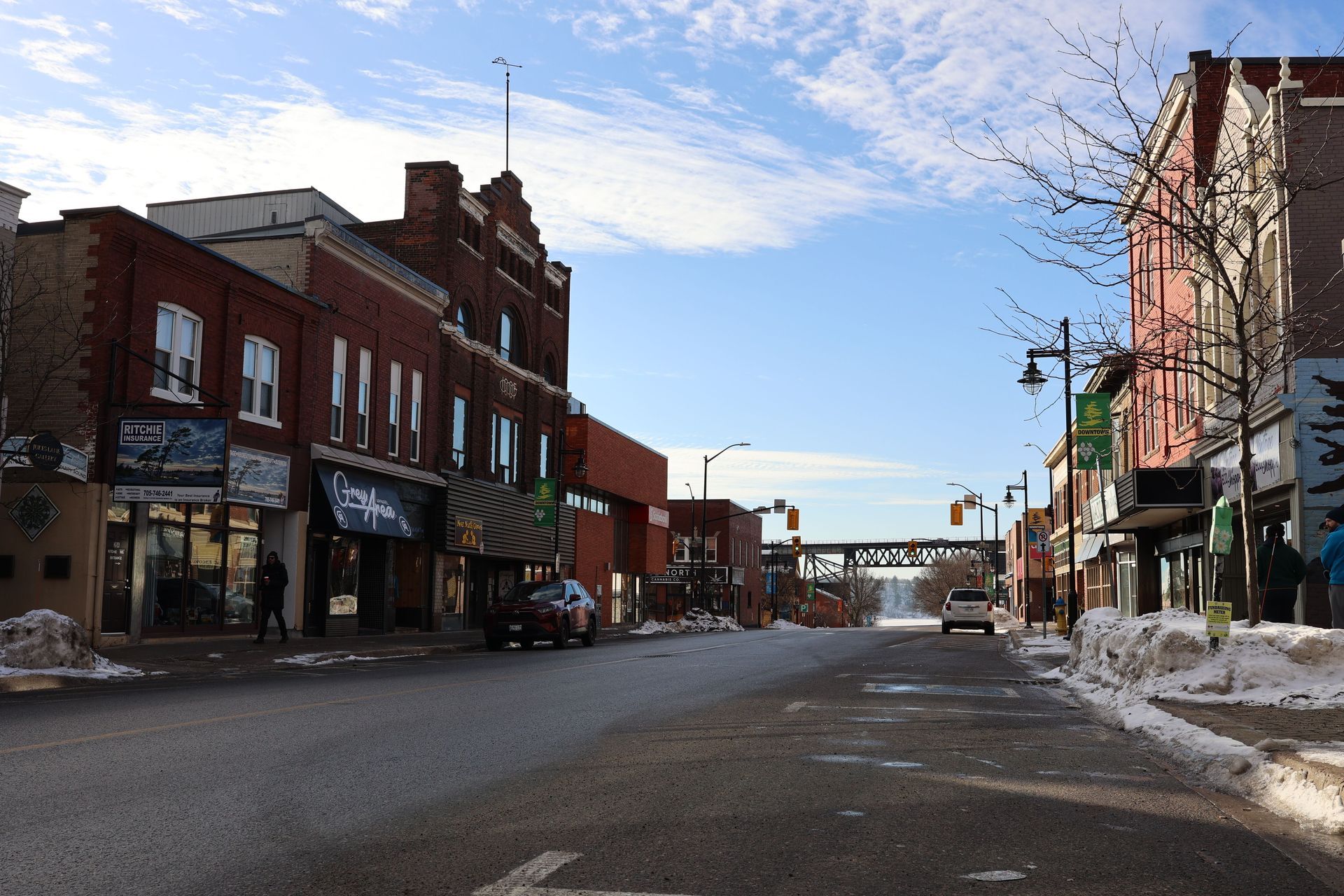 Snowy downtown street lined with brick storefronts under a partly cloudy sky