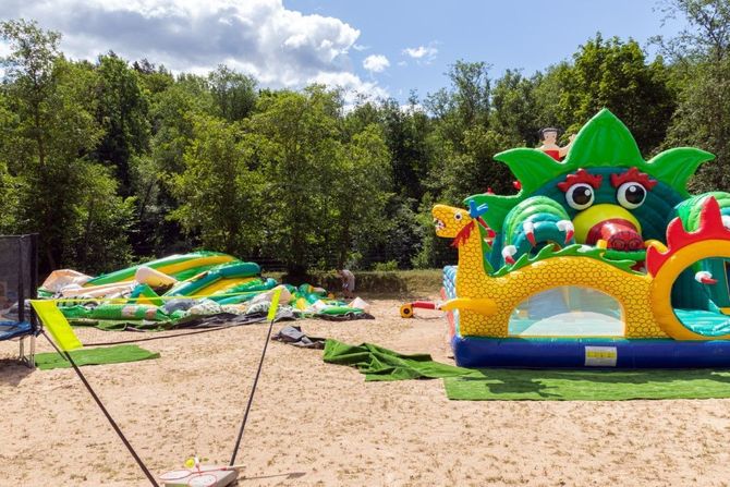 Colorful inflatable water slide and bounce house on a sandy beach with trees in the background