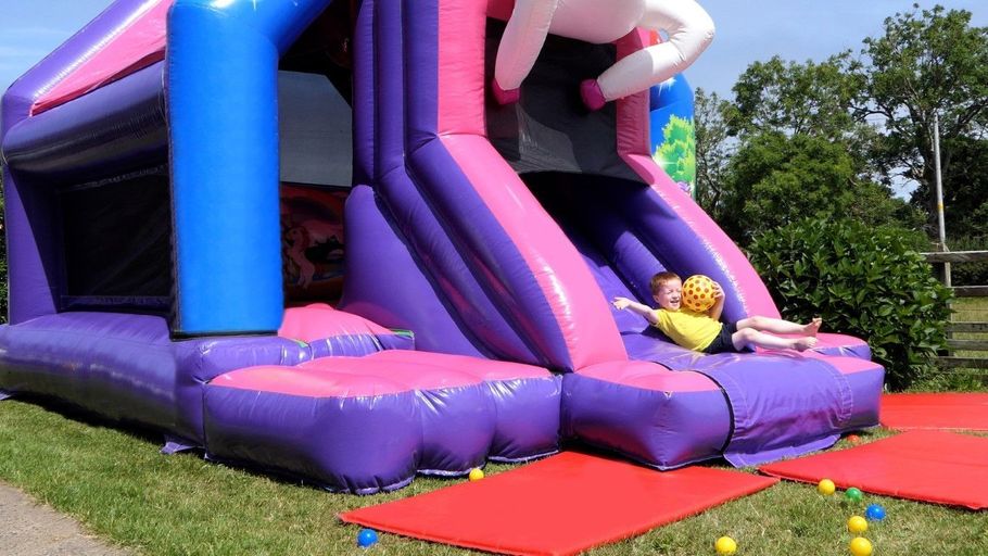 Colorful inflatable slide in a park with a child at the bottom and a red mat in front