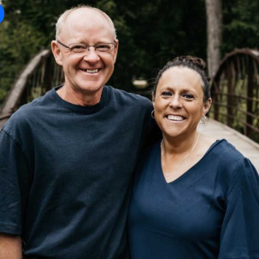 Smiling couple in dark blue shirts standing on a bridge in a wooded park Smiling couple in dark blue shirts standing on a bridge in a wooded park