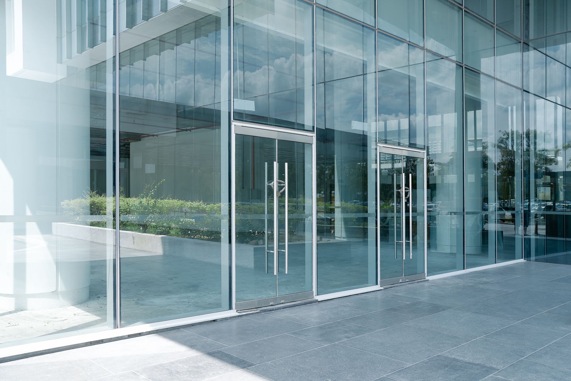 Glass building entrance with clear glass walls and doors, reflecting the sky.