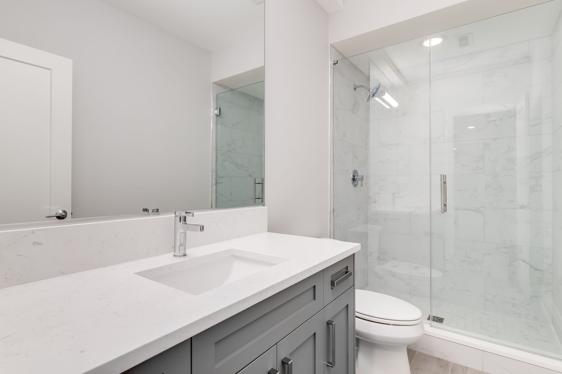 Modern bathroom with gray vanity, white countertop, and glass shower.