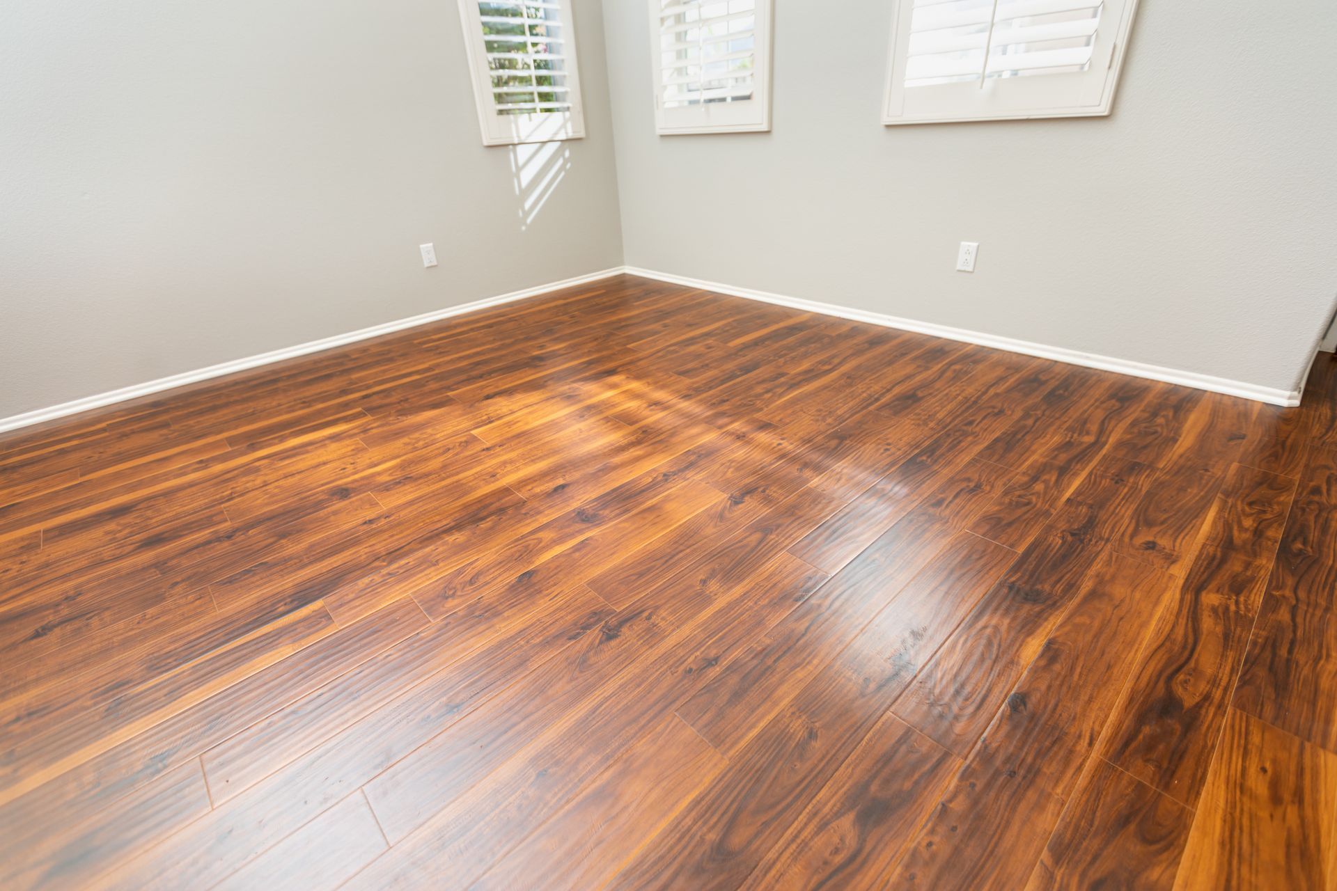 Empty room with glossy, dark wood floor and gray walls. Three windows with closed white shutters.