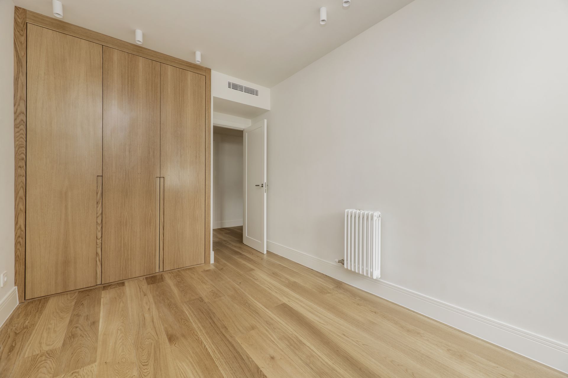 Empty room with wooden floors, white walls, large wooden closet, and a doorway.