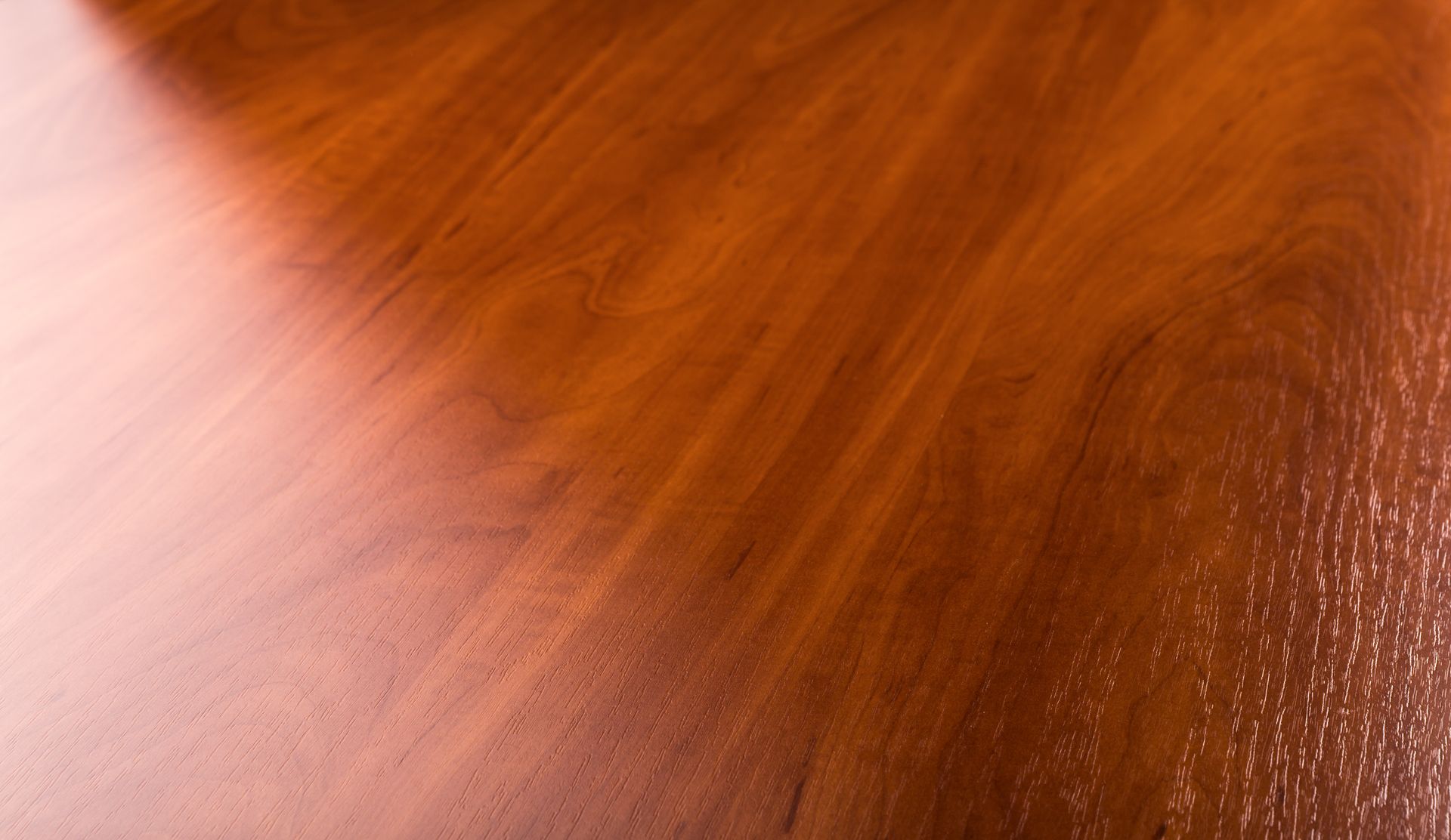Close-up of polished, reddish-brown wooden surface with visible wood grain and light reflections.