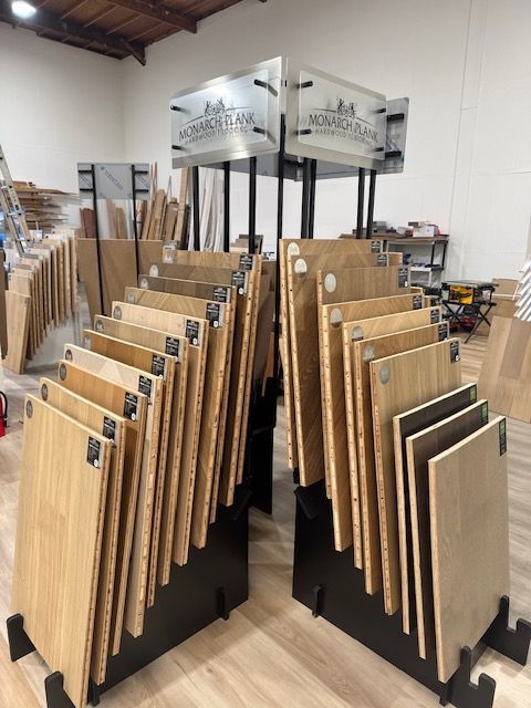 Rows of wood flooring display samples in a showroom with large stand signs overhead.