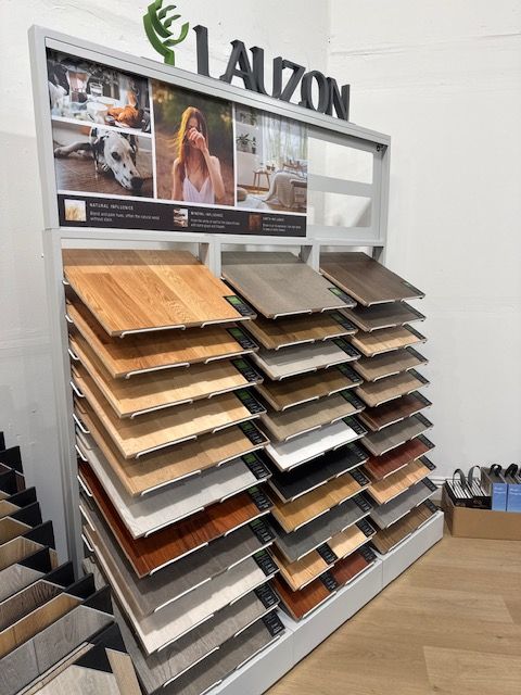 Alzon flooring display with stacked sample planks in a showroom, showing various wood and tile finishes