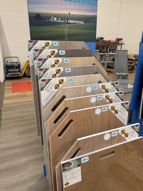 Wood flooring samples displayed on angled racks in a showroom with carpet and flooring posters in back.